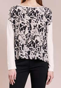 Długi rękaw top z czarnym kwiatowym wzorem na beżowym tle, z gładką białą okrągłą szyją i obrzeżem. Gładka tekstura tkaniny.