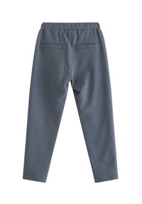 Grijze taps toelopende broek met een elastische tailleband en twee achterzakken, van achteren getoond op een plain witte achtergrond.