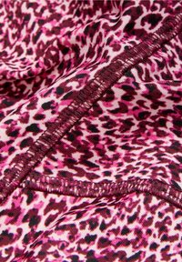 Pink og lilla leopardprintstof med glat tekstur, der har en mørk syet søm langs kanten og variationer i mønsterets tæthed.