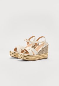 Beige wedge sandals with a textured woven heel and gold accents. Features cross straps and a buckle closure.