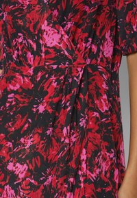 Vestido floral con base negra con patrones en acuarela en tonos rojos y rosas, diseño cruzado y textura de tela suave.