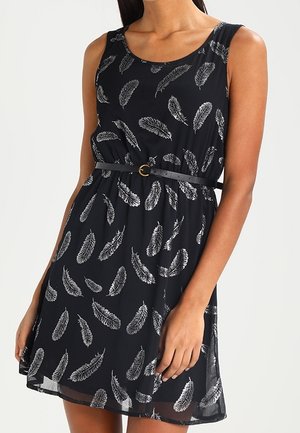 Robe noire sans manches avec un motif de plumes blanches, cintrée à la taille avec une fine ceinture noire présentant une petite boucle ronde dorée.