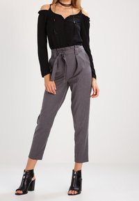 Černá top bez ramínek s knoflíky, kombinovaný s šedými kalhotami s vysokým pasem a opaskem. Model nosí černé boty na podpatku s otevřenou špičkou.