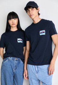 Mørkeblå T-shirts med korte ærmer har en lomme med et stribet mønster og bæres med lyseblå højtaljede jeans. Casual stil.