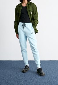 Light blue sweatpants with pockets, black drawstring, and Nike logo, paired with a black tank top and green button-up shirt, and black shoes.