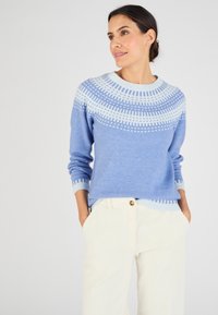 Pull bleu clair en tricot doux, avec un design à motif sur le plastron en blanc, col rond et poignets côtelés. Associé à un pantalon en velours côtelé crème.