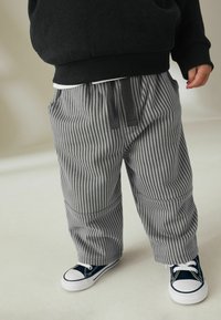 Grå og hvide stribede bukser med en afslappet pasform, der har en elastisk talje og lommer, parret med navy sneakers.