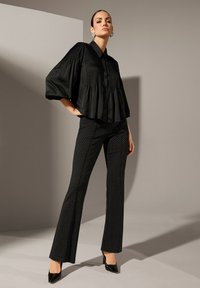 Zwarte satijnen blouse met plooien en knoopsluiting, gecombineerd met een fitted zwarte broek met witte stippen en een uitlopende pijp.