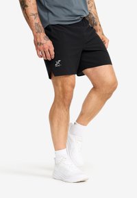 Black athletic shorts made of lightweight fabric, featuring a logo on the left hem, and side slits for added mobility.