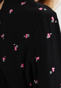 Un tissu noir présente un motif éparpillé de formes en rose, gris et imprimé animal. Le design est texturé et léger avec une finition douce.