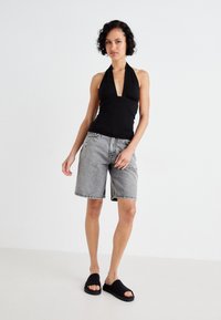 Svart halterneck med samlet detalj, parret med grå denimshorts og svarte klippsandaler. Minimalistisk design med en avslappet passform.