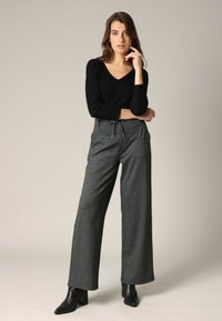 Zwarte langarmtop met een V-hals, gecombineerd met hoge, wijde grijs gestreepte broek en zwarte hoge hak enkellaarzen.
