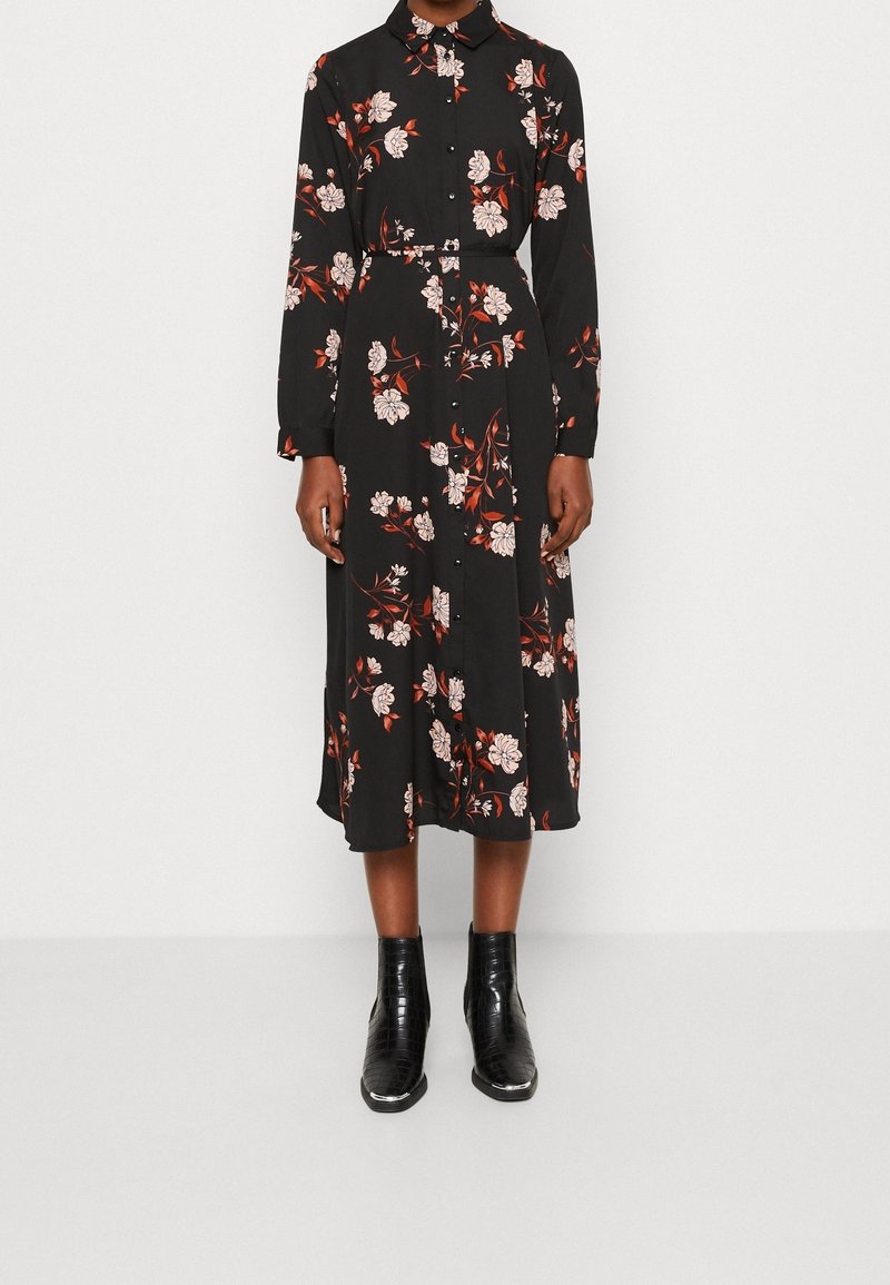Robe chemise midi noire à manches longues avec imprimé floral rouge et blanc, associée à des bottines noires.