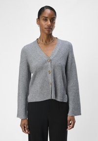 Grå cardigan med V-hals, ribbestruktur og tre treknapper foran. Har lange ermer og kort passform.