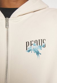 Krémová mikina na zip se textem "PEOUS" a grafiku modrého akvarelového koně. Texturovaná tkanina s předním zipem.