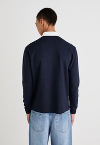 Camisa de manga larga azul marino con cuello blanco, hecha de un material suave. Presenta un diseño sencillo y un ajuste relajado, combinada con unos jeans de color azul claro.