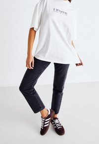 Camiseta blanca de gran tamaño con el logo "LEVI'S", combinada con jeans gris oscuro y zapatillas burdeos con rayas blancas y suelas marrones.
