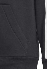 Schwarzer Sweatshirt mit Kängurutasche, gerippten Bündchen und strukturiertem Stoff, mit kontrastierenden weißen Streifen entlang des Ärmels.