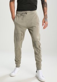 Hellgraue Jogginghosen aus weichem Stoff, mit verstärkten Knieflicken, elastischem Bund mit Kordelzug und schmalen Bündchen.