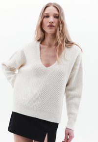 Maglione a coste color crema, con scollatura a V profonda, vestibilità rilassata e spalle basse, abbinato a una mini gonna nera.