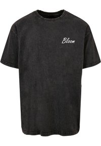 Camiseta de algodón negra con cuello redondo y mangas cortas. Presenta la palabra "Bloom" bordada en blanco en el lado izquierdo del pecho. Corte clásico.