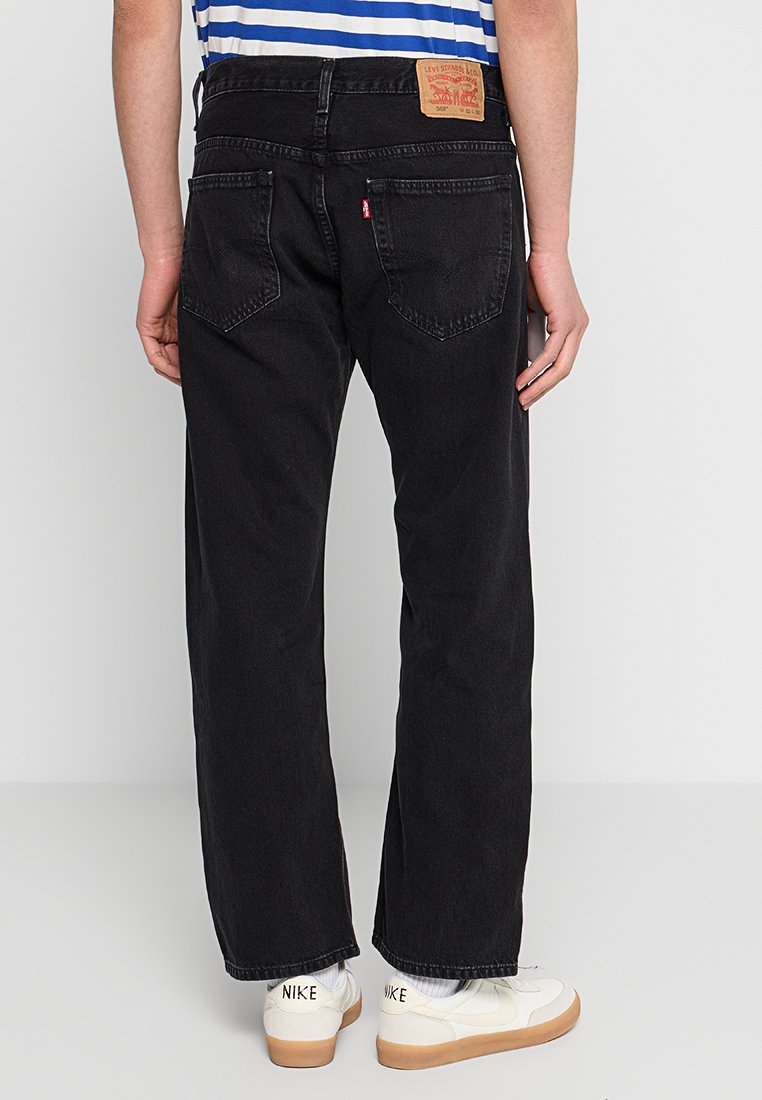 Czarne jeansy o prostych nogawkach wykonane z denimu, z tylnymi kieszeniami oraz skórzaną naszywką z logo na pasku. W połączeniu z białymi sneakersami.