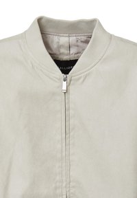 Giacca bomber beige chiaro con colletto a costine e una cerniera frontale argentata, mostrata dalla parte superiore del petto al colletto.