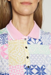 Kragepolo skjorta med ett färgglatt lapptäckesmönster i rosa, blått, grönt och gult; fem svarta knappar framtill.