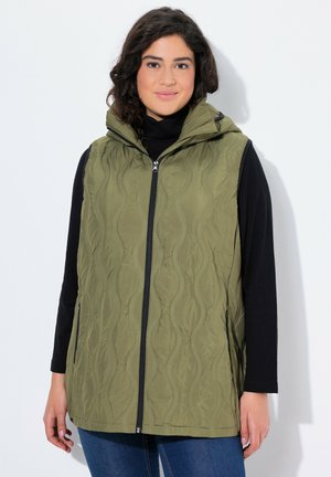 Chaleco acolchado verde oliva con capucha, que presenta un cierre frontal, bolsillos laterales y un patrón de ondas texturizado. Llevado sobre una camiseta negra de manga larga.