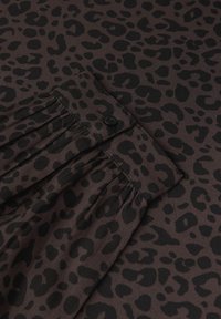 Brauner Stoff mit schwarzen Leopardenflecken; umfasst einen Knopf und weiche Falten, die eine strukturierte Oberfläche mit einem unverwechselbaren Muster schaffen.