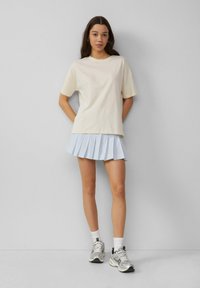 T-shirt en coton beige clair à manches courtes, associé à une mini-jupe plissée bleu clair. Porté avec des chaussettes blanches et des baskets argentées.