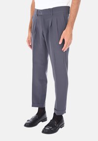 Pantaloni grigi a pieghe con taglio dritto e orlo con risvolto. Il tessuto ha una texture liscia; abbinati a mocassini neri e calzini scuri.