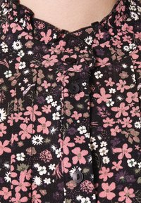 Schwarzer Blumenstoff mit rosa, weißen und grünen Blumenmustern, in einem plissierten Design und mit schwarzen Knöpfen entlang des vorderen Ausschnitts.