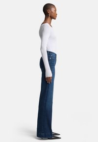 Jeans in denim a vita alta, gamba dritta, di colore blu scuro con un classico design a cinque tasche. Abbinati a un top a maniche lunghe bianco aderente.