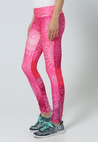 Leggings rosa con motivi intricati, caratterizzati da una combinazione di tonalità chiare e scure, un elastico alto in vita e un dettaglio con zip alla caviglia.