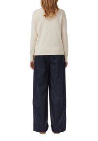Maglione a maglia beige abbinato a pantaloni a gamba larga navy con righe sottili. L'outfit presenta una vestibilità rilassata e una texture morbida.