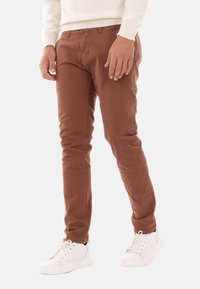 Chinos in cotone marrone con una vestibilità slim, caratterizzati da una trama liscia e tasche laterali, abbinati a sneaker bianche.