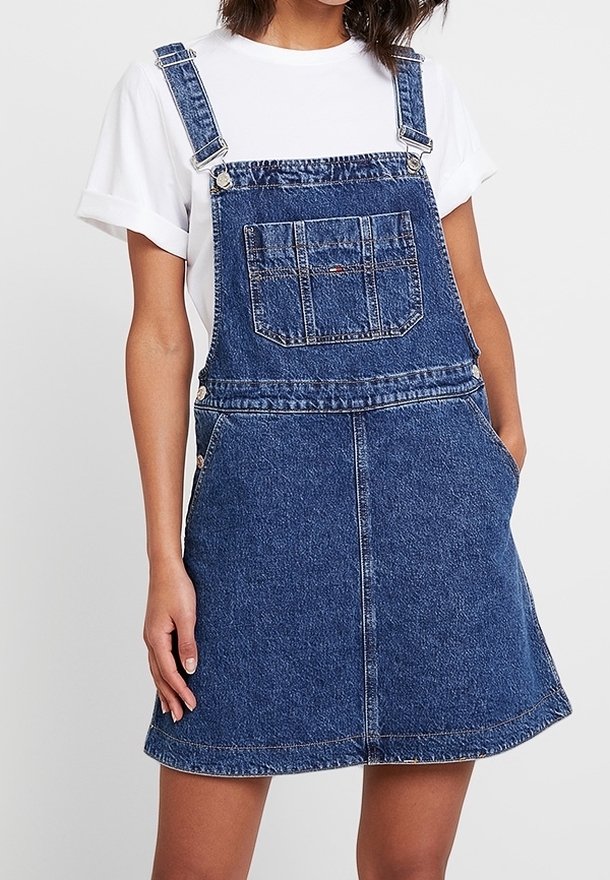 Vestido de tirantes de mezclilla en azul oscuro con tirantes ajustables, bolsillo frontal y falda acampanada. Textura suave y acentos de costura mínima.