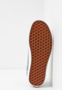 Sole boty s texturovaným hnědým gumovým povrchem s diamantovým vzorem, lemovaná bílým materiálem a šedým horním okrajem.