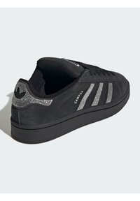Crna antilop tenisica s tri metalik srebrne pruge, ukrašenim peta s rhinestone kamenčićima i gumenim potplatom s teksturiranim prianjanjem.
