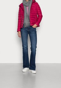 Punainen toppatakki hupulla, harmaa huivi ja vaaleanpunaraitainen paita, yhdistetty sinisiin levenevälahkeisiin farkkuihin ja valkoisiin tennareihin neutraalilla taustalla.