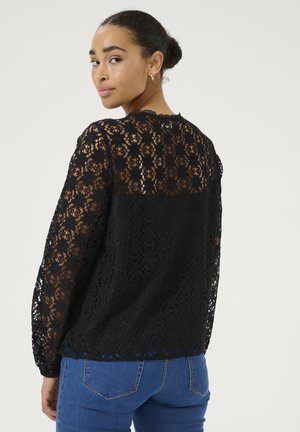 Haut long en dentelle noire avec un motif floral, un tissu texturé, un col festonné et un dos noir uni. Assorti avec un jean bleu.