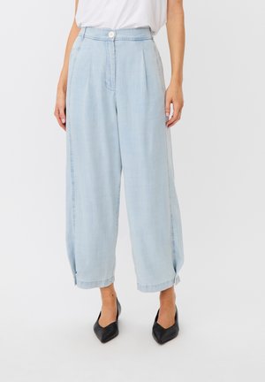 Kobieta nosząca jasnoniebieskie, szerokie spodnie z wysokim stanem i podwiniętymi nogawkami, obuwie na czarnych, spiczastych obcasach, w połączeniu z białym topem.