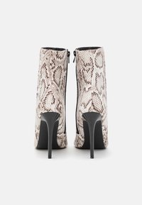 Botins de salto alto com padrão de cobra, apresentando material sintético texturizado em branco e castanho, fecho de zíper preto e saltos agulha.