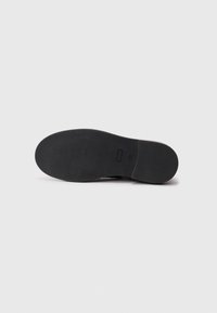 Semelle de chaussure en caoutchouc noire avec un motif texturé et un design plat, arborant un logo minimal près du talon. Des bords lisses définissent la forme.