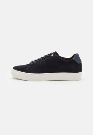 Mørkeblå ruskinds sneakers med en hvid gummisål. Har runde snørebånd, forstærket hæl og diskrete stikninger langs overdelen.