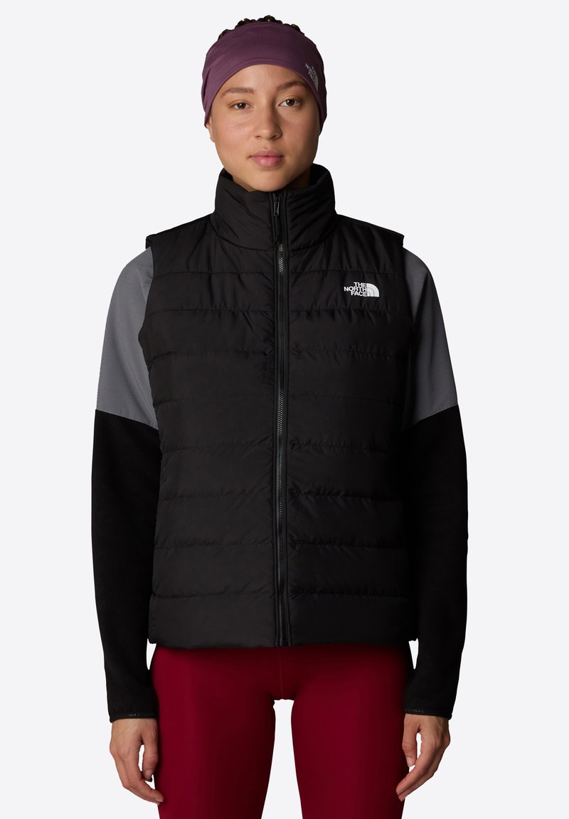 Svart puffervest med glidelås foran, quiltet design, og The North Face-logo. Grå langermede skjorter og tettsittende røde bukser fullfører antrekket.