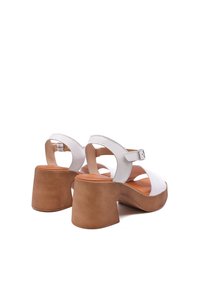 Sandali beige in pelle con tacco, dotati di un design con aperture, cinturino regolabile alla caviglia e tacco a blocco di un marrone chiaro. Texture liscia e stile minimalista.