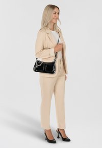 Beige op maat gemaakt pak met een slanke pasvorm en taps toelopende broek, gecombineerd met een zwarte laarzenhandtas met een metalen kettingdetail.