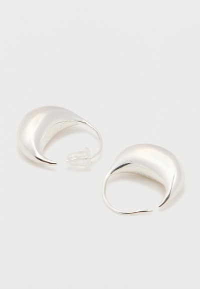 Par de pendientes de aro en forma de media luna pulidos en plata con cierres de plástico transparente sobre una superficie blanca.